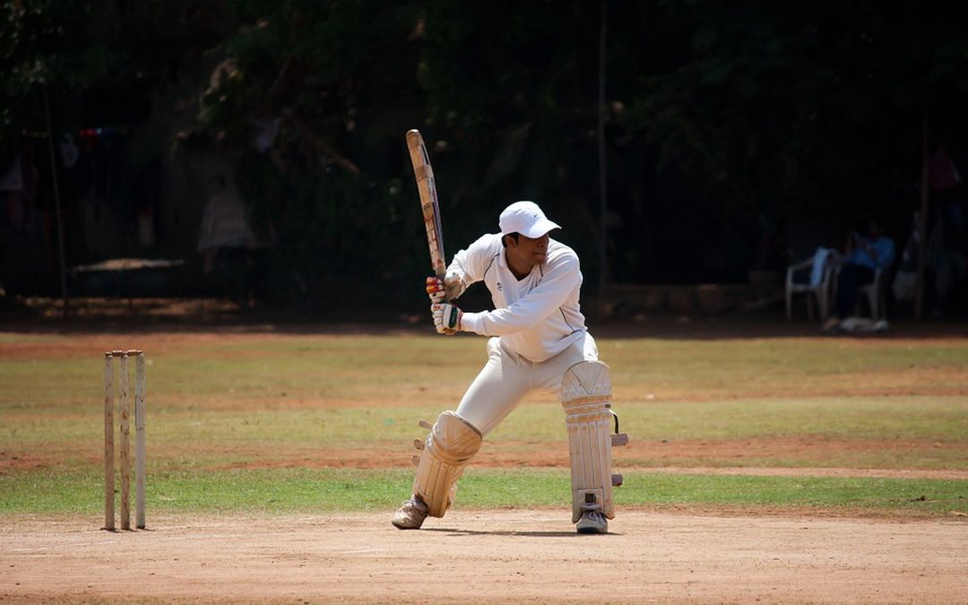 Cricketspeler slaat bal het speelveld uit, door het voorraam van zijn auto